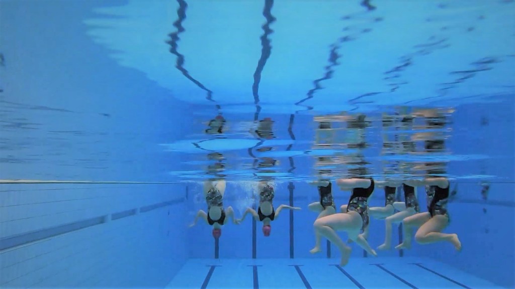 An underwater view of Edinburgh Synchro swimmers performing a combo routine - some swimmers doing a figure, others doing arm movements
